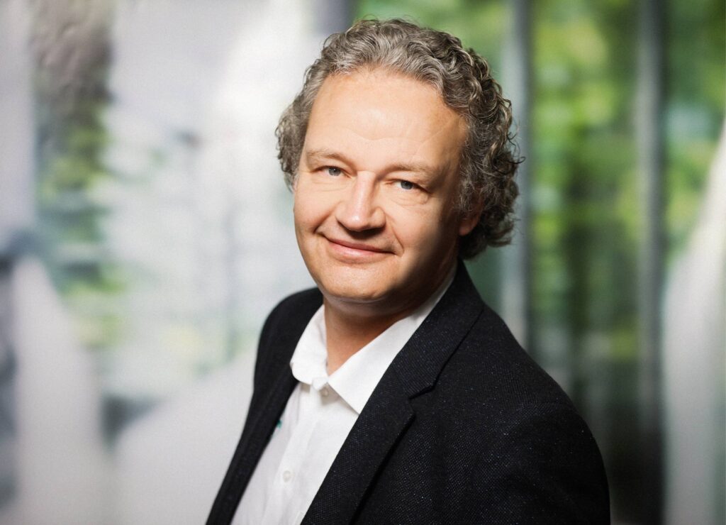 Porträt eines Mannes mittleren Alters in Businesskleidung vor unscharfem Hintergrund.